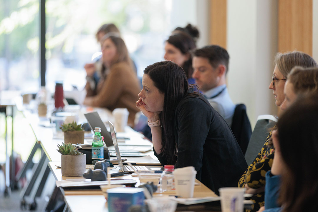 A woman leaning in to listen to a panelist at a table of people