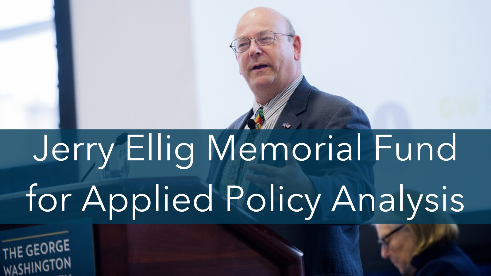 Jerry Ellig at a podium with a text banner over his image that reads "Jerry Ellig Memorial Fund for Applied Policy Analysis"