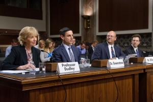 Jerry Elleig testifying at a government hearing; Name plates at the table read Professor Dudley, Dr. Greenstone, and Dr. Elling 